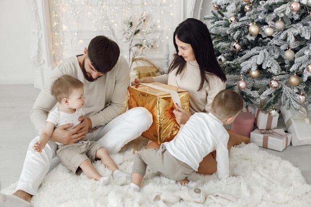 Jeune famille en vêtements blancs assis près de l'arbre de Noël