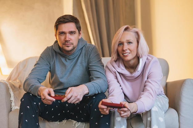 Jeune famille en vêtements de maison jouant à des jeux vidéo sur un canapé dans le salon