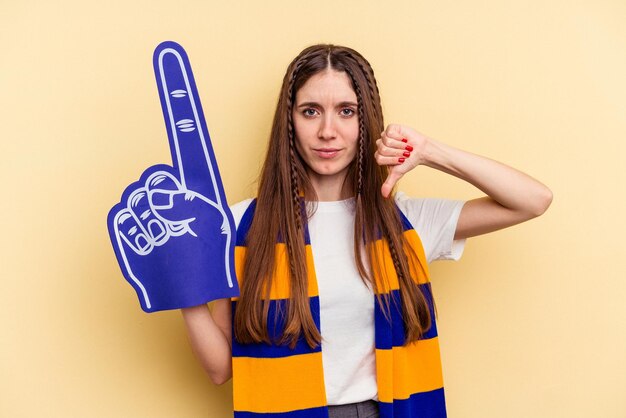 Jeune fan de sport femme isolée sur fond jaune montrant un geste d'aversion pouce vers le bas Concept de désaccord