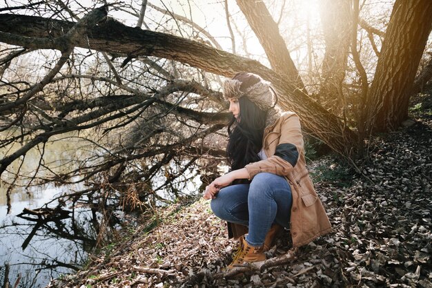 Une jeune femme accroupie contre des arbres en automne.