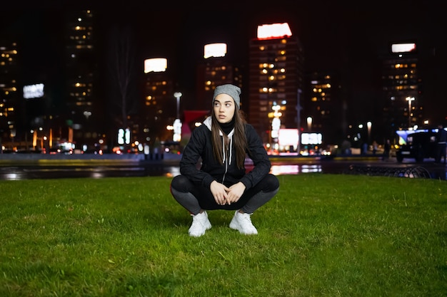 Jeune femme accroupie tout en se préparant pour la formation en plein air de nuit dans une grande ville