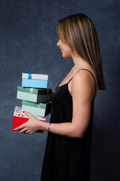 Une jeune femme a acheté des cadeaux du Nouvel An et les tient dans ses mains sur un fond sombre Vacances en famille