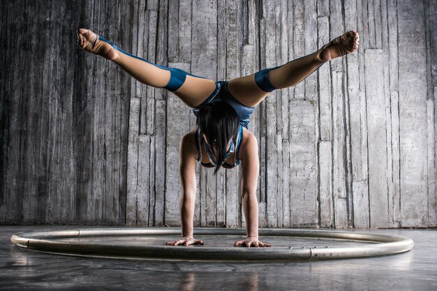 Jeune femme acrobate debout sur la main sur une surface grise en studio photo