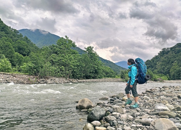 Jeune femme active avec sac à dos au fond des montagnes et de la rivière