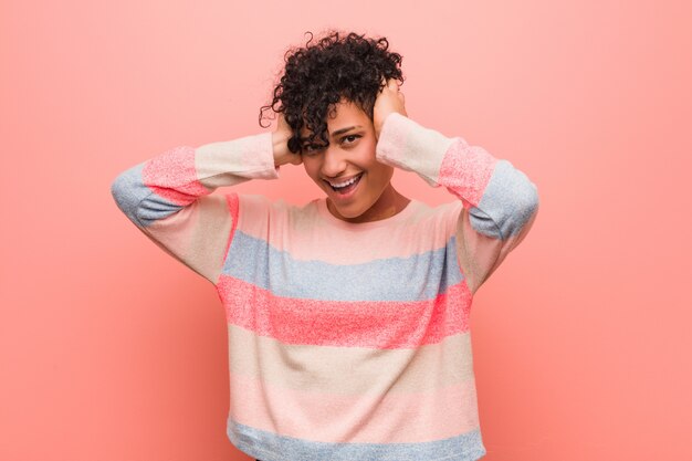 Jeune femme adolescente afro-américaine mixte rit joyeusement en gardant les mains sur la tête. Concept de bonheur.