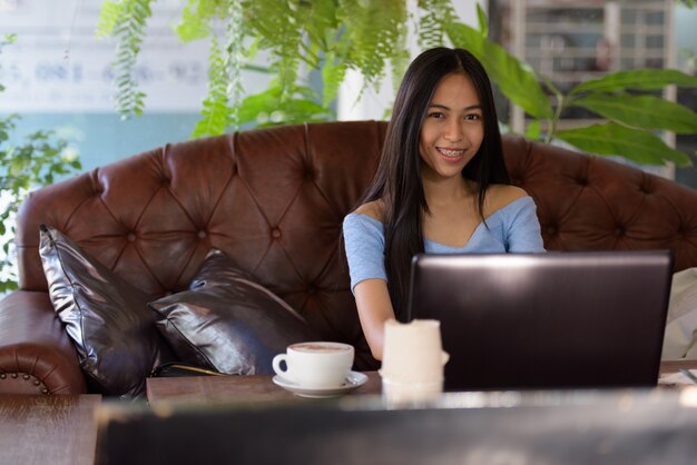 Jeune femme adolescente asiatique heureuse au café en plein air avec ordinateur portable