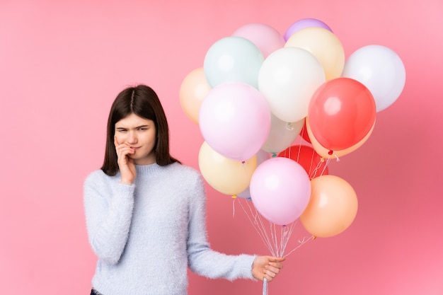 Jeune femme adolescente ukrainienne tenant beaucoup de ballons sur le mur rose isolé nerveux et effrayé