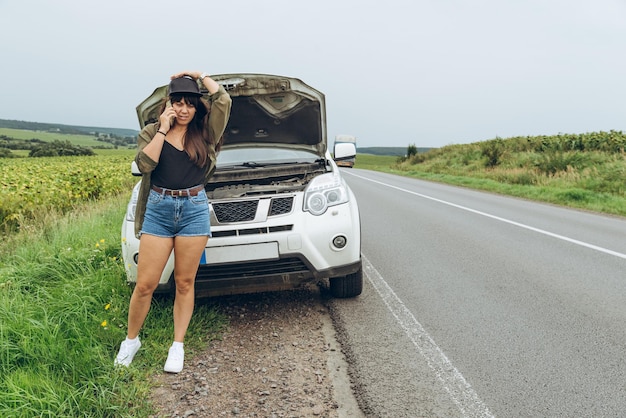 Jeune femme adulte debout près d'une voiture cassée sur l'autoroute et parler