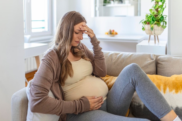 Jeune femme adulte enceinte reposant sur un canapé à la maison se sentant mal