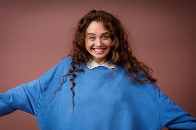 Une jeune femme adulte heureuse portant un pull bleu printemps à l'intérieur regardant la caméra avec un sourire joyeux