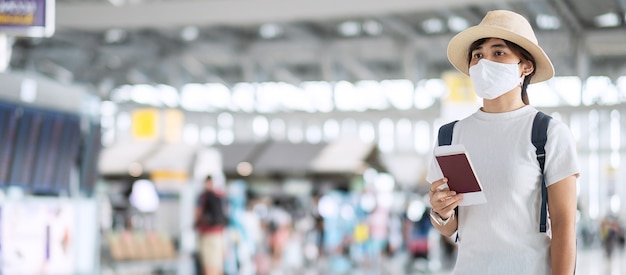 Jeune femme adulte avec masque facial tenant un passeport dans le terminal de l'aéroport