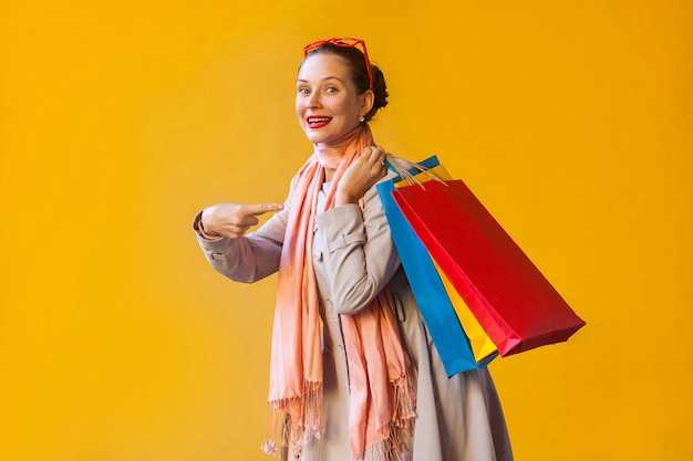 Jeune femme adulte pointant le doigt sur les sacs et regardant la caméra et le sourire à pleines dents. Sur fond jaune. Prise de vue en studio