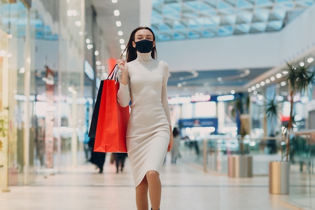 Jeune femme adulte portant un masque médical protecteur portant des sacs en papier dans les mains dans un magasin de détail