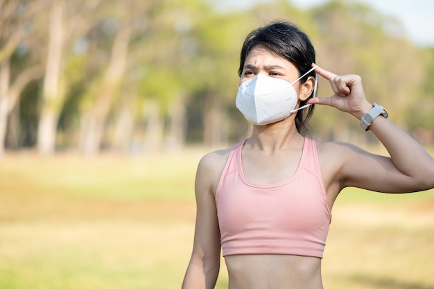 Jeune femme adulte portant un masque protecteur N95 pendant l'étirement musculaire dans le parc en plein air