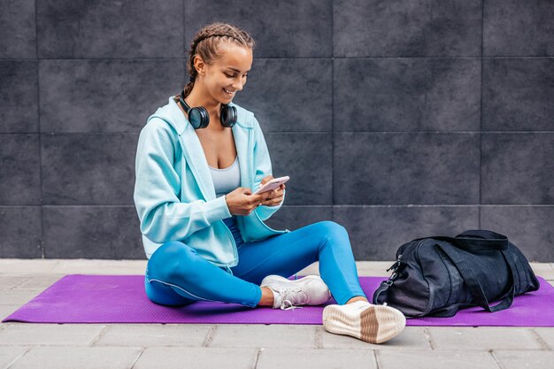 Jeune femme adulte relaxante après l'entraînement physique. Elle est assise et utilise son téléphone intelligent pour communiquer avec quelqu'un.