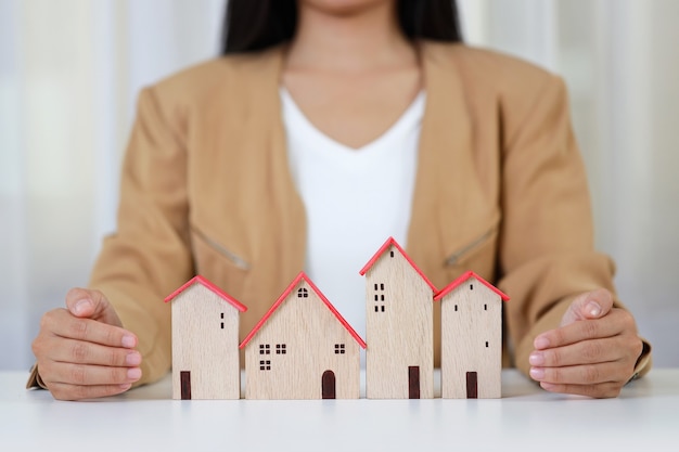 Jeune femme d'affaires actives mains en tenue décontractée assis et protégeant le modèle de maison sur le tableau blanc.