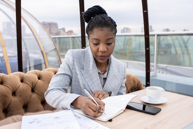 Jeune femme d'affaires africaine élégante écrivant le plan de travail