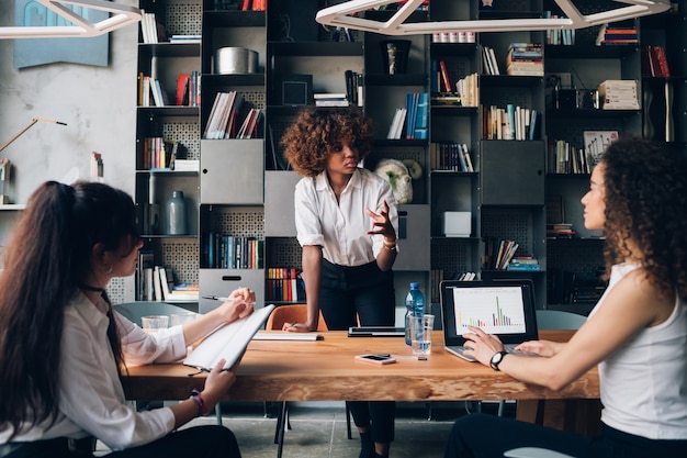 Jeune Femme D'affaires Africaine En Interaction Avec Des Collègues Dans Le Bureau De Co-working Et Travaillant Sur Le Projet