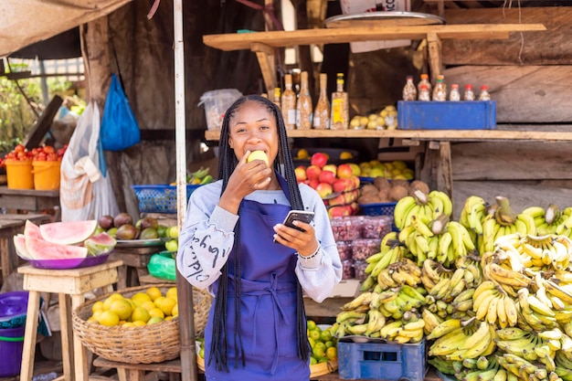 Jeune femme d'affaires africaine noire sur un marché local naviguant en ligne à l'aide d'un smartphone vérifiant la lecture des nouvelles en ligne