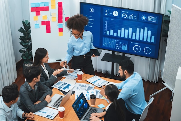 Une jeune femme d'affaires africaine présente un tableau de bord d'analyse de données sur l'écran de télévision dans une réunion moderne Présentation d'affaires avec un groupe d'hommes d'affaires dans la salle de conférence Concord