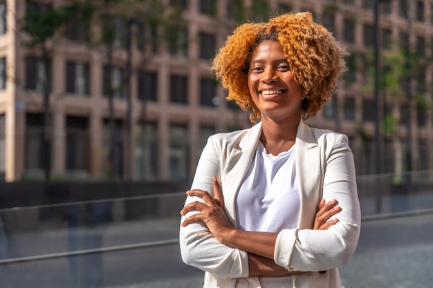 Une jeune femme d'affaires africaine se tient fière avec les bras croisés à l'extérieur.