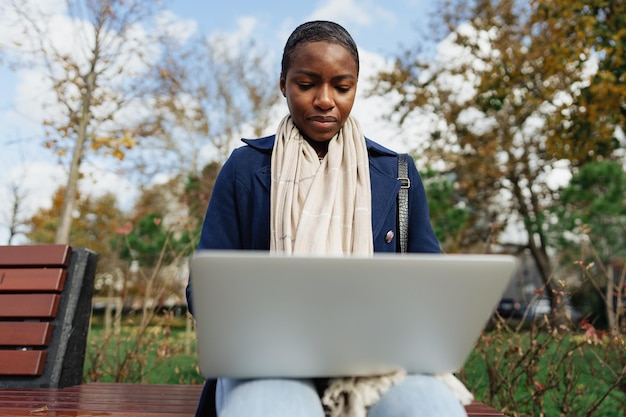 Jeune femme d'affaires africaine utilisant un ordinateur portable assis sur le banc dans la ville