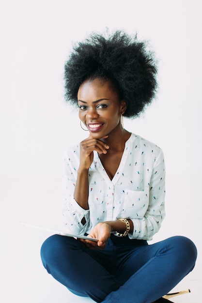 Jeune femme d'affaires afro-américaine à l'aide de la tablette tout en étant assis sur le sol, isolé sur blanc