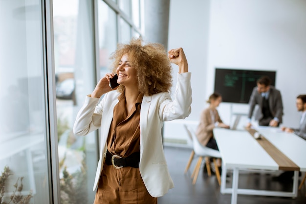 Photo jeune femme d'affaires afro-américaine debout et à l'aide de téléphone mobile dans le bureau moderne