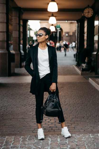 jeune femme d'affaires afro-américaine élégante en veste rester à la ville et tenir un sac.