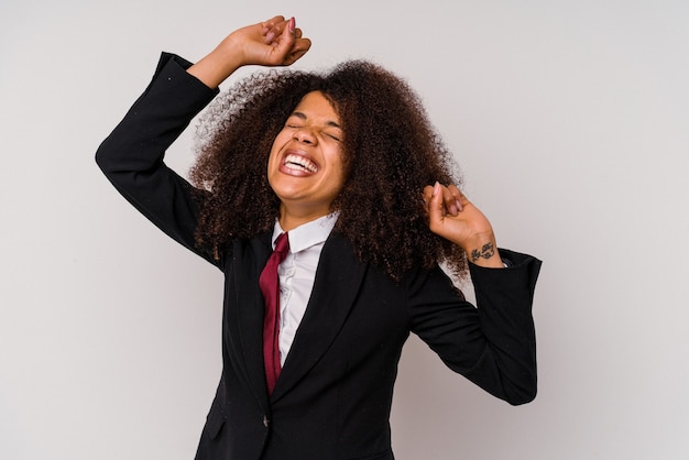 Jeune femme d'affaires afro-américaine portant un costume isolé sur blanc célébrant une journée spéciale, saute et lève les bras avec énergie.