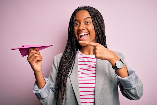 Jeune femme d'affaires afro-américaine tenant un avion en papier comme symbole de communication très heureux pointant avec la main et le doigt