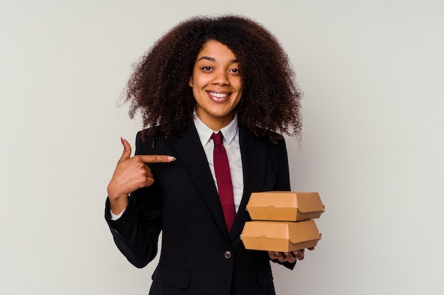 Jeune femme d'affaires afro-américaine tenant un hamburger isolé sur blanc personne pointant à la main vers un espace de copie de chemise, fier et confiant