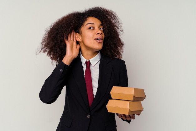 Jeune Femme D'affaires Afro-américaine Tenant Un Hamburger Isolé Sur Fond Blanc En Essayant D'écouter Un Commérage.