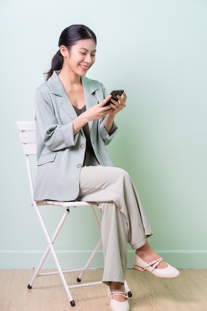 Jeune femme d'affaires asiatique assise sur une chaise sur fond vert