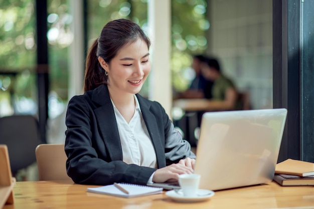 Jeune femme d'affaires asiatique belle charmante souriant et utilisant un ordinateur portable au bureau