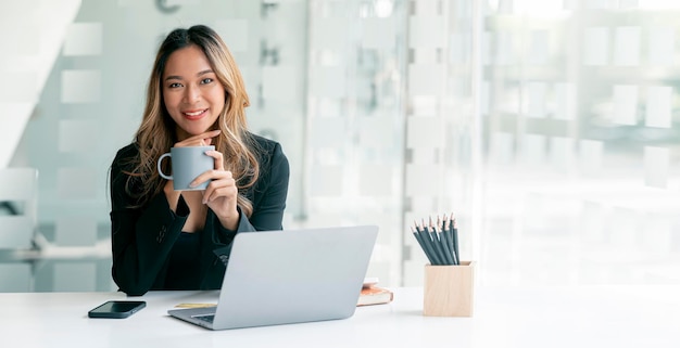 Jeune femme d'affaires asiatique belle charmante souriante et regardant la caméra assis au bureau