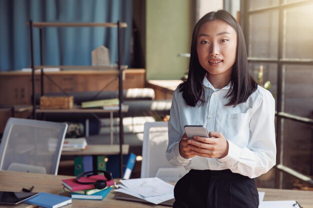 Jeune femme d'affaires asiatique debout au bureau et tenant le téléphone