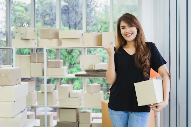 Jeune femme d'affaires asiatique heureux porte un emballage de boîte de colis et montre le succès de l'entreprise