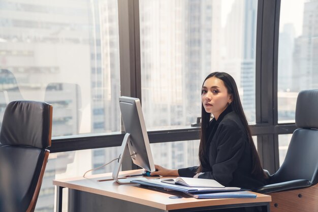 Jeune femme d'affaires asiatique intelligente adulte en costume décontracté noir travaillant avec un ordinateur dans un bureau urbain