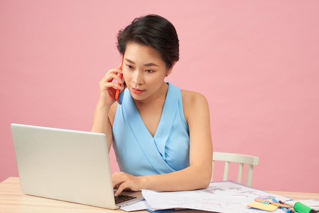 Jeune femme d'affaires asiatique parlant au téléphone et travaillant sur un ordinateur portable