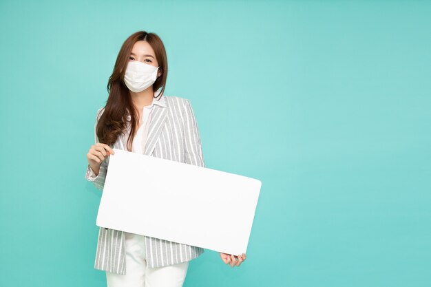 Jeune femme d'affaires asiatique portant un masque facial et montrant la tenue de panneau d'affichage blanc vierge isolé sur fond vert