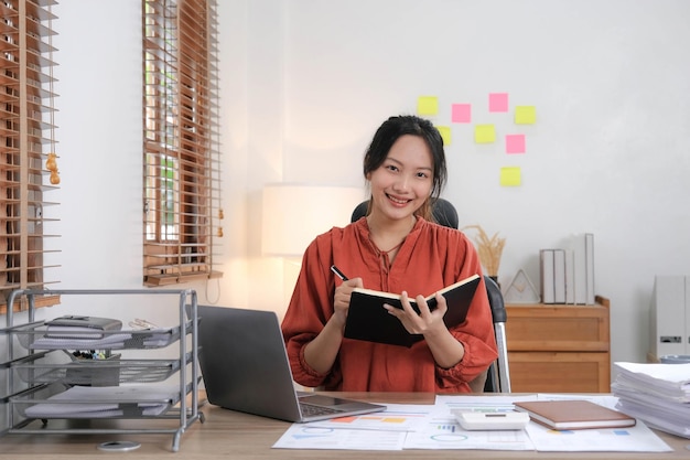 Jeune femme d'affaires asiatique prenant des notes à l'aide d'un ordinateur portable au bureau moderne