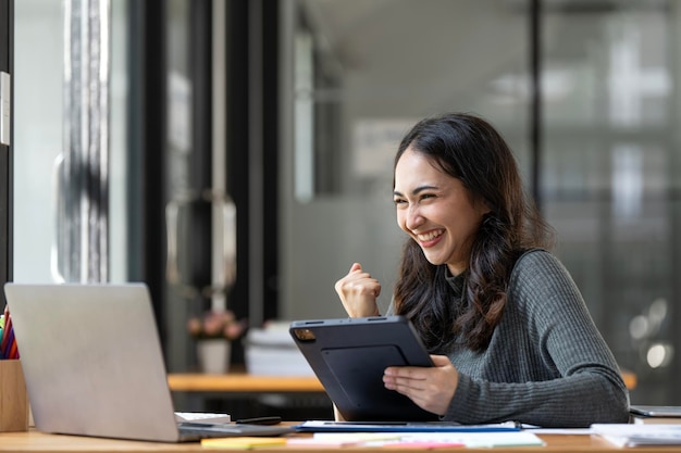 Jeune femme d'affaires asiatique prospère atteignant des objectifs excités avec un ordinateur portable au bureau