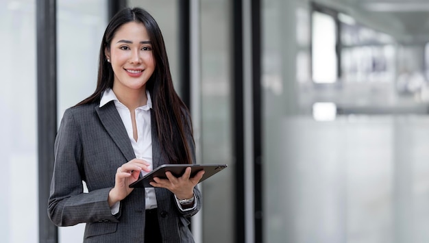 Jeune femme d'affaires asiatique regardant la caméra tenant une tablette au bureau