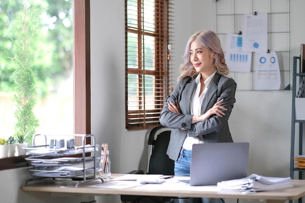 Jeune femme d'affaires asiatique souriante et confiante, chef d'entreprise prospère, chef de la direction de l'entreprise professionnelle élégante, femme d'affaires asiatique est debout au bureau avec les bras croisés