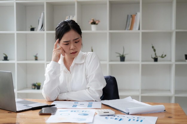 Une jeune femme d'affaires asiatique stressée et épuisée qui a mal à la tête à cause d'une mission surchargée.