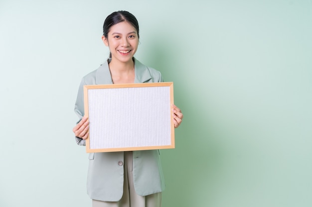 Jeune femme d'affaires asiatique tenant un tableau blanc sur fond vert