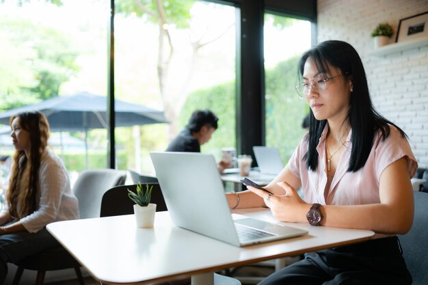 Une jeune femme d'affaires asiatique travaille avec un ordinateur portable et un téléphone portable dans un café.