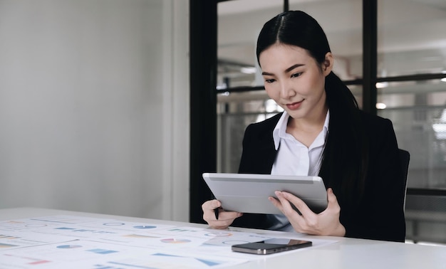 Une jeune femme d'affaires asiatique travaille sur une tablette avec un ordinateur portable au bureau