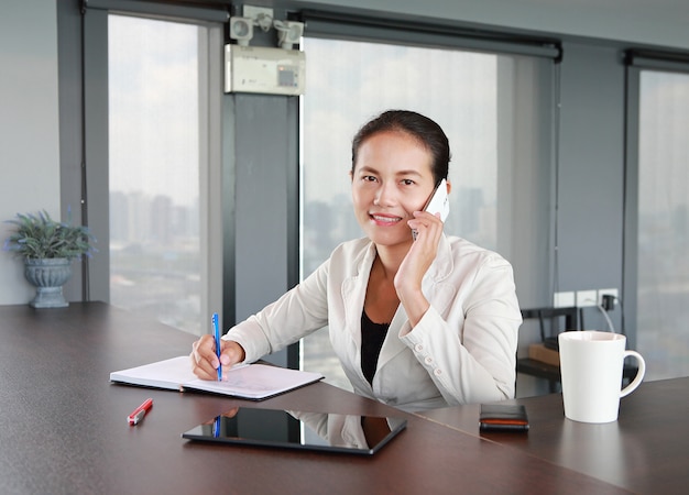 Jeune femme d&#39;affaires assis à la table sur le lieu de travail au bureau à l&#39;aide du téléphone